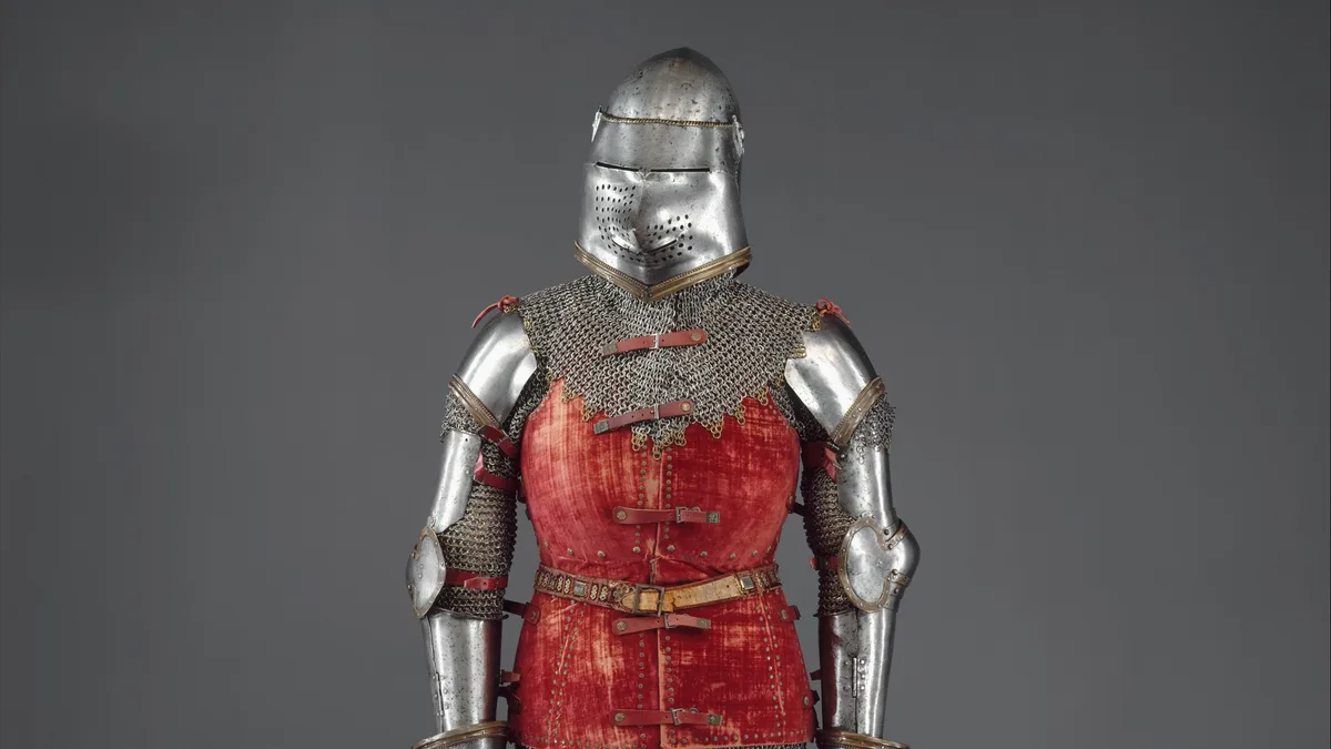 Armadura de caballero medieval con peto rojo y cota de malla sobre fondo gris
